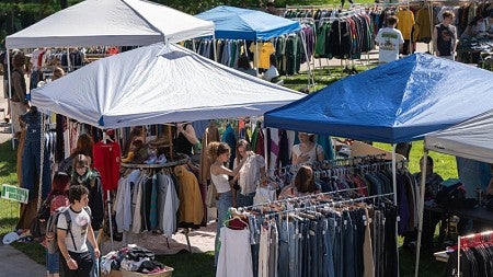 Shoppers peruse stalls filled with clothes at the UO Flea Market during a sunny day