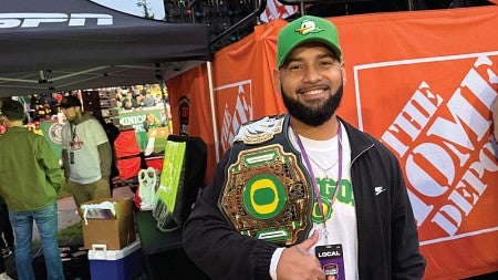 MBA student Les Rodriguez stands holding a University of Oregon champion belt over his shoulder