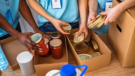 Close up photo of three people's hands as they fill boxes with food items