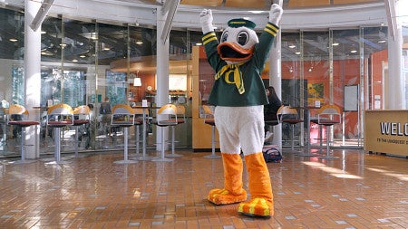 The UO Duck mascot raises its arms above its head in celebration