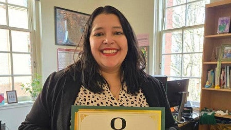 Lorena Landeros smiles as she holds up an award plaque