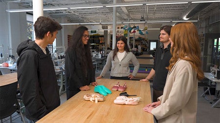 The student members of a Sports Product Management project team chat together while looking over several paires of ballet pointe shoes laid out on the table before them