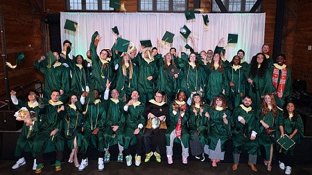 SPM students, wearing commencement regalia, throw their caps into the air