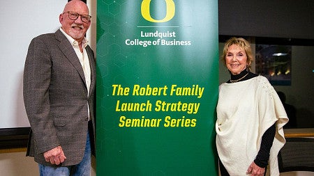 Ned Robert and Carol Ezeir stand beside a banner bearing the text -The Robert Family Launch Seminar Series-