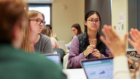 Two students sitting at a table looking at someone across from them.