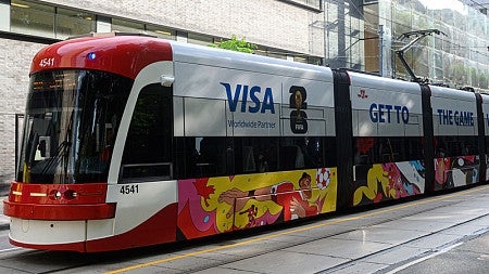A tram on a Toronto street is emblazoned with art of football players and VISA branding