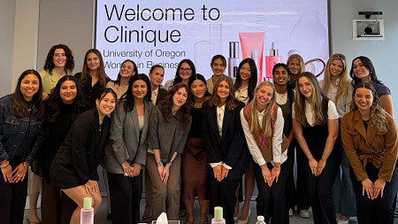 Members of the Women in Business Club pose for a group photo in front of a projection screen reading -Welcome to Clinique-