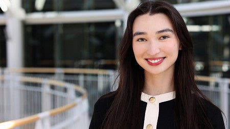 Young woman smiles. She has long black hair and is wearing a black and white sweater with gold buttons. 