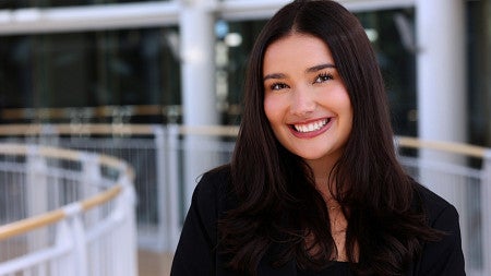Young woman smiles at the camera. She has long dark hair and is wearing a black blazer and black shirt.