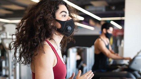 A person exercises on a gym treadmill while wearing a mask