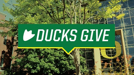 DucksGive logo against a background image of the Lillis Business Complex