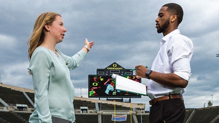 Two students talk on the field of a sports arena