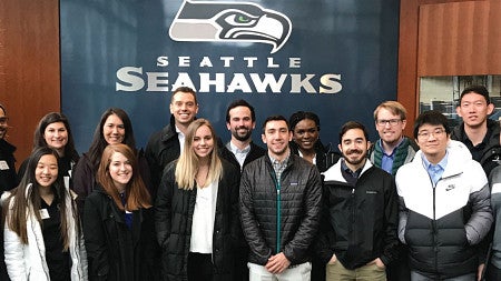 MBA students take a group photo in front of the Seattle Seahawks logo