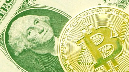 Coin representation of BitCoin atop a dollar bill