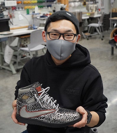 SPM student Yoshimi Saito holds a custom designed high-top shoe he made in the SPM lab while wearing a mask