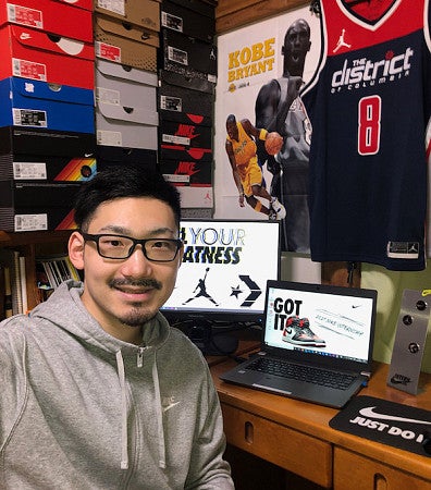 SPM student at his internship for a sports product company with stack of shoe boxes behind his computer, a Kobe Bryant poster, and a basketball jersey on the wall