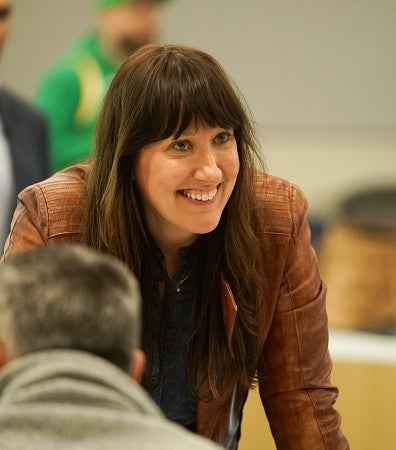 Close-up of Rachel McGinn standing in a classroom, leaning over a desk, smiling at someone outside the frame.