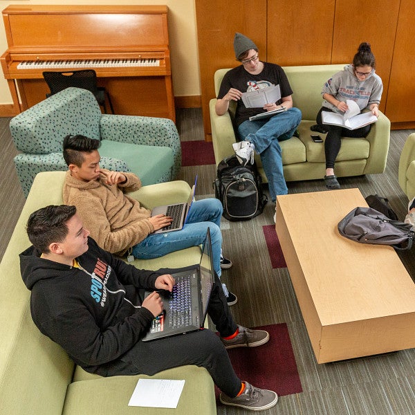 Group of students sitting on sofas studying and talking in the Business Academic Residential Community.