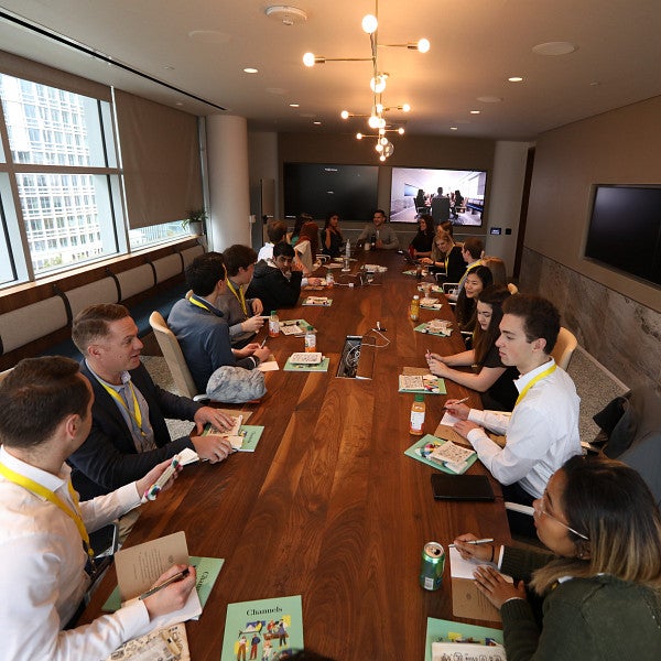 Several students sitting around a conference table talking with industry experts