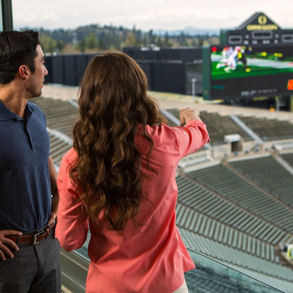 Two students in the control booth looking over the field at Autzen Stadium.
