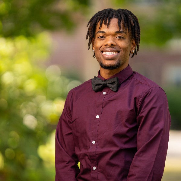 Student Jurell Scott standing and smiling at the camera with trees in the background.