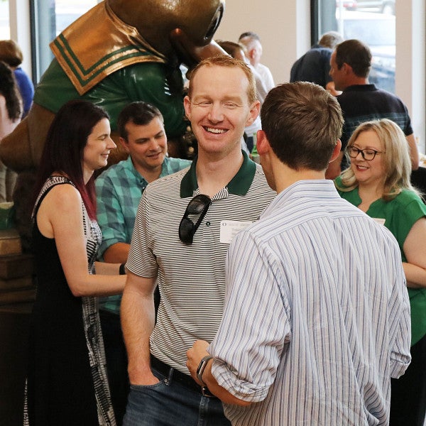 Several alums standing near a statue of the Duck mascot, smiling and talking.