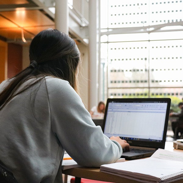 Student sitting at a table with their back to the camera, working on a project on a laptop.