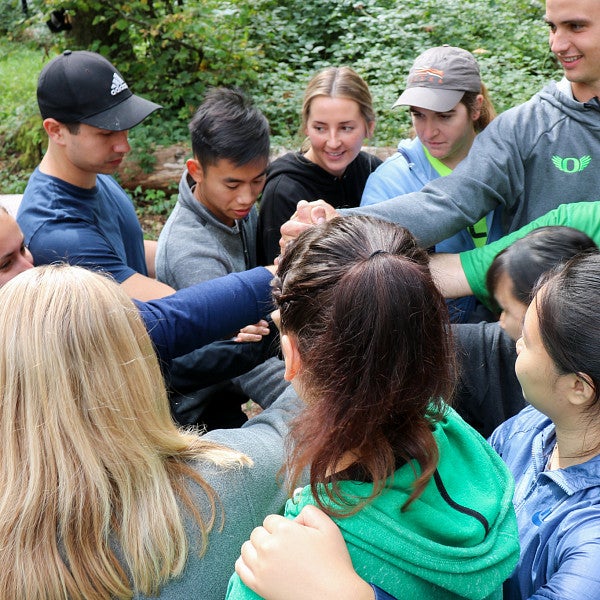 Group of students standing in a circle outside clasping hands in the center of the circle