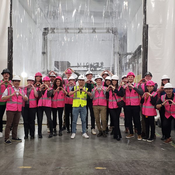 Students standing in a large group wearing hard hats and safety vests while visiting a factory