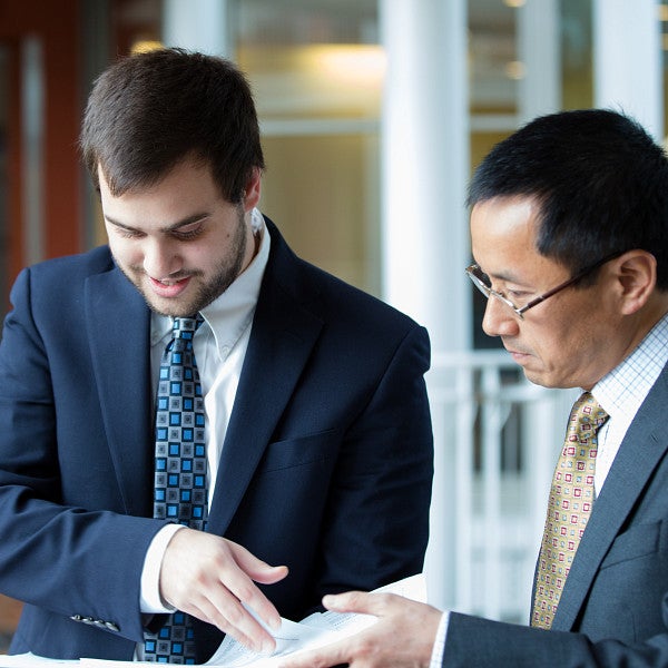 A student and professor standing in the hallway looking down at papers the student is holding