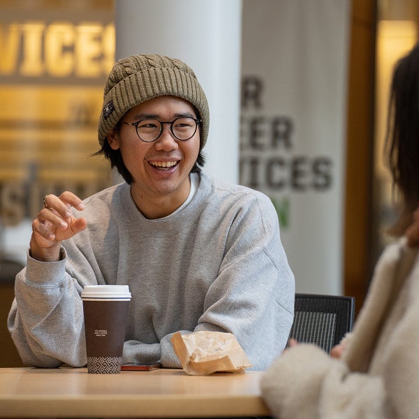 Two students sitting at a table with coffee looking at each other and smiling