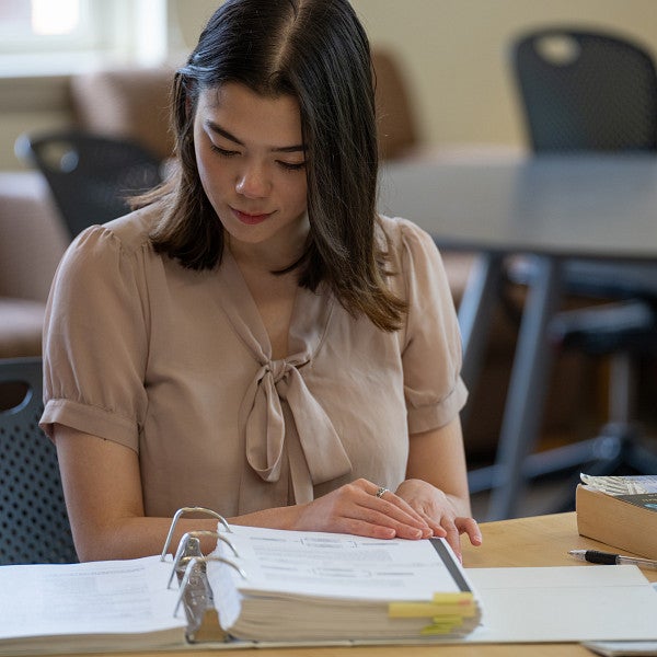 Student sitting at a table, looking down at a 3-ring binder and study books