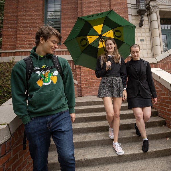 Three students walking down the steps outside of Anstett Hall while talking to each other and one student holds an umbrella