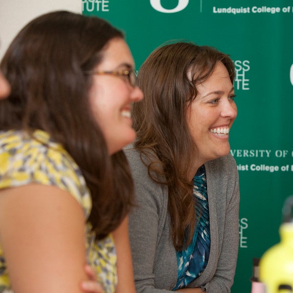 Three students sitting at a table with laptops smiling and looking off-camera