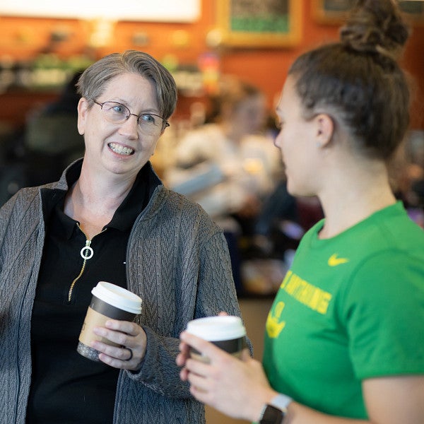 Faculty members standing with a student drinking coffee and talking