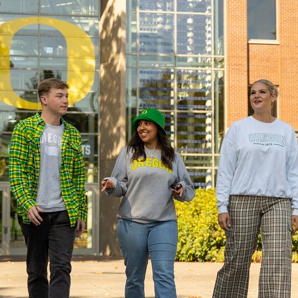 A small group of students walking outside towards the camera in front of the Lillis Business Complex and talking to each other.