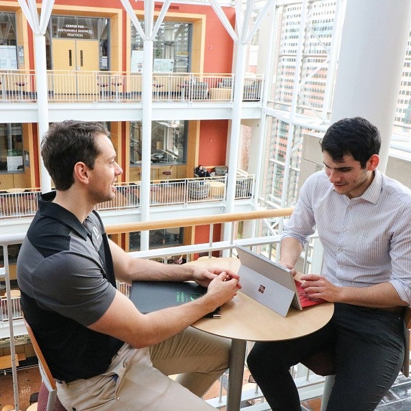 Two students sitting at a table in the Lillis atrium with laptops, smiling and talking to each other