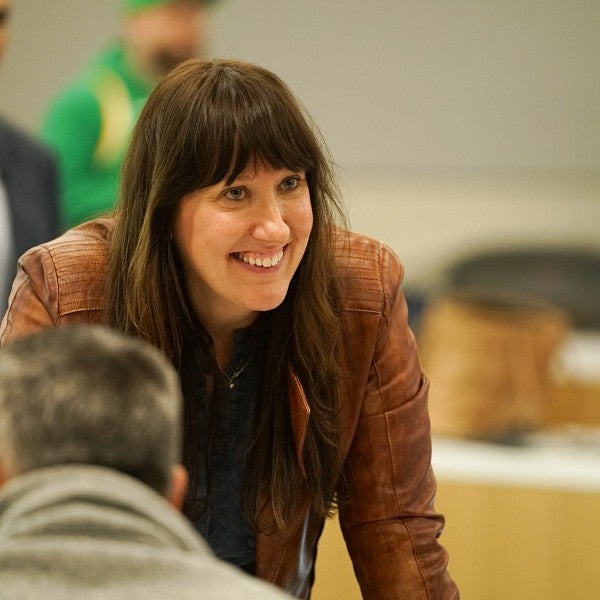 Close-up of Rachel McGinn standing in a classroom, leaning over a desk, smiling at someone outside the frame.