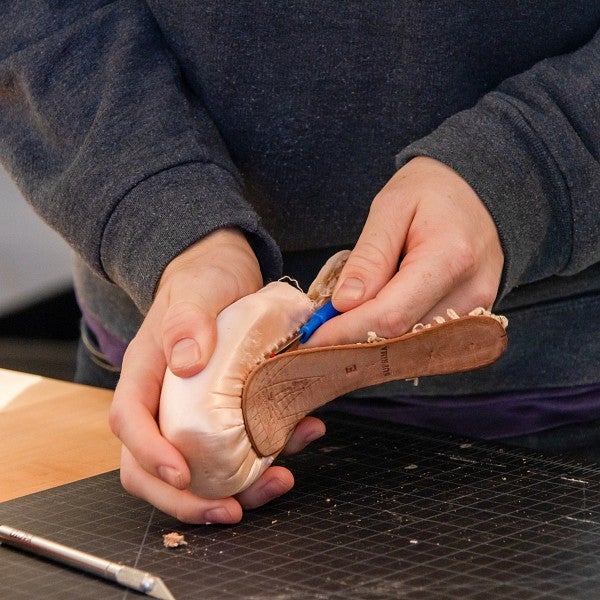 A close-up of a student's hands working with tools on a shoe mold.