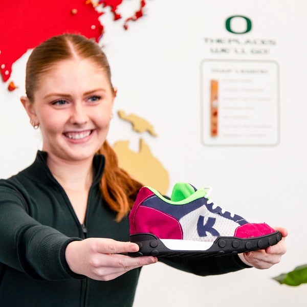 A close-up of a student smiling and holding a shoe towards the camera.