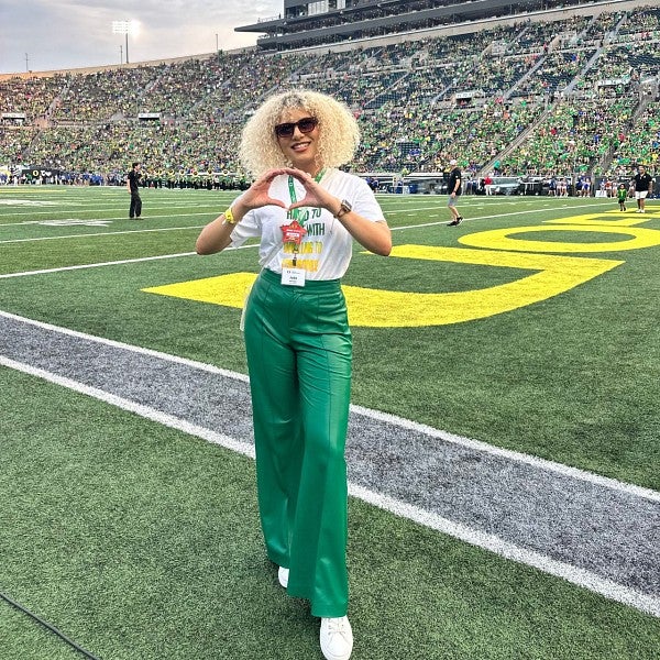 Lundquist College alum Jada Allender makes the "O" symbol with her hands as she stands on the field of a packed Autzen Stadium