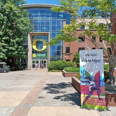 A photo of the south entrance to the Lillis Business Complex taken while the Track & Field World Athletics Championships Oregon22 where being held at the university. A vertical banner stands outside the building advertising the event.